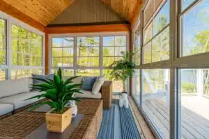 A cozy enclosed porch conversion with large windows and a wooden ceiling.