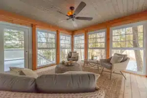 Cozy enclosed porch with WeatherMaster™ Windows, wicker furniture, and a ceiling fan, offering a warm retreat with a wintery outdoor view.