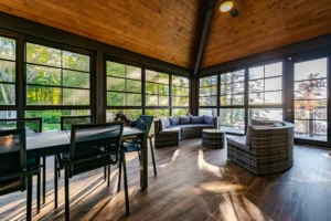 A cozy enclosed porch conversion with large windows and a wooden ceiling.