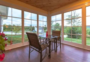 A cozy enclosed porch conversion with large windows and a wooden ceiling.