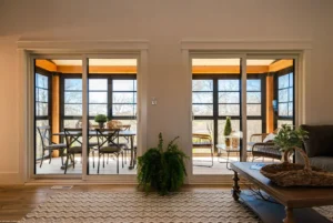 Enclosed porch conversion with sliding glass doors, black-framed windows, and cozy seating.