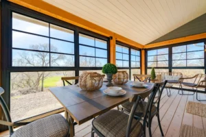 A cozy enclosed porch conversion with large windows and a wooden ceiling.