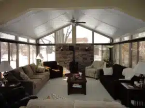 Cozy interior of a Insulated Sunroom with large glass windows, comfortable seating, and a central stone fireplace.