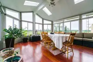 Spacious Insulated Sunroom with panoramic windows, wooden flooring, and a dining setup.