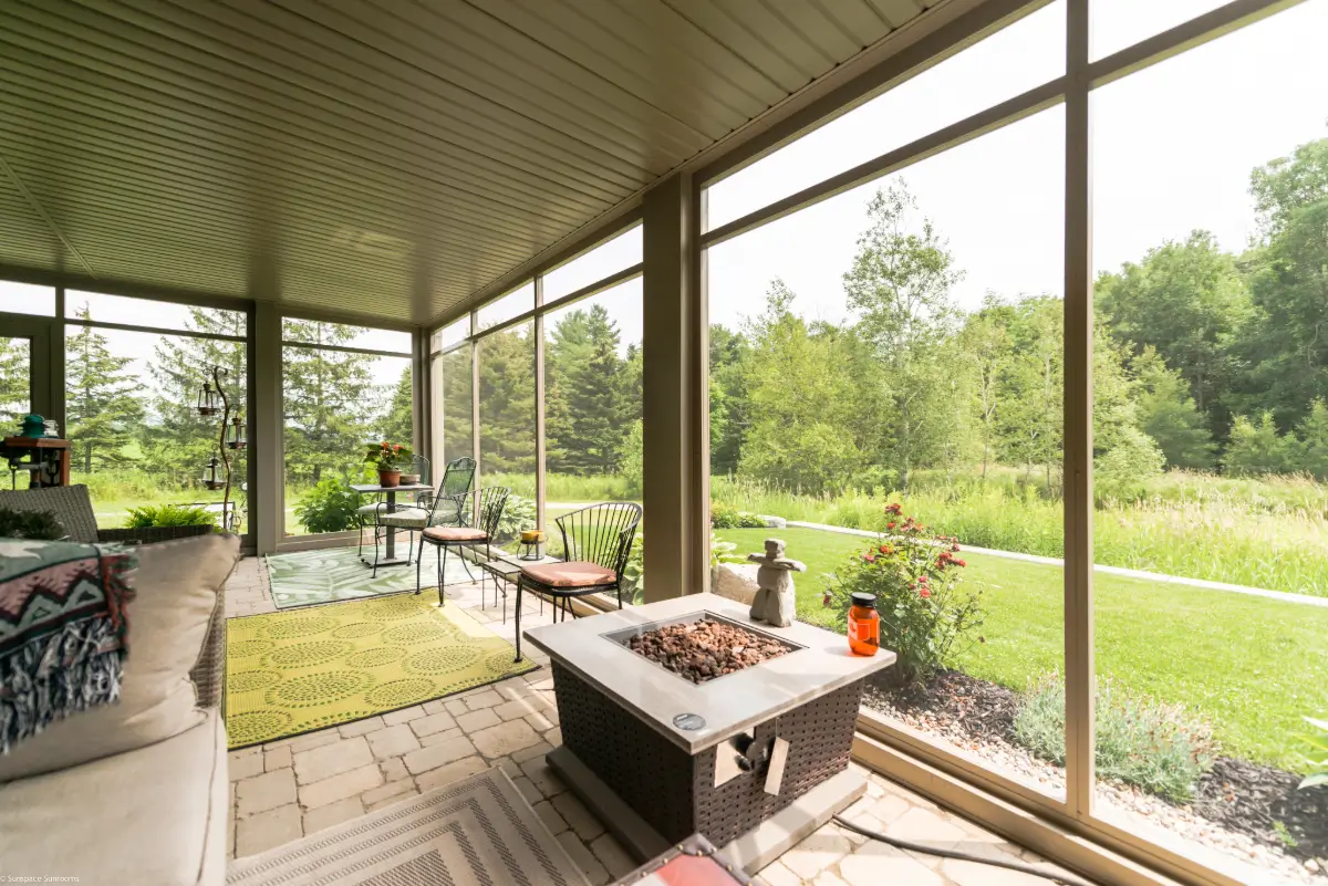 A beautifully designed screen room with a solid roof, mesh walls, and outdoor furniture, offering a cozy and bug-free relaxation space with a scenic garden view.