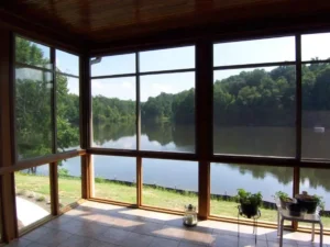 Sunroom with large WeatherMaster™ Horizontal windows offering a clear view of a scenic lake and lush greenery, creating a bright and airy space.