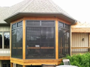A stylish octagonal sunroom with WeatherMaster™ Windows, framed in wood, attached to a house with a shingled roof.