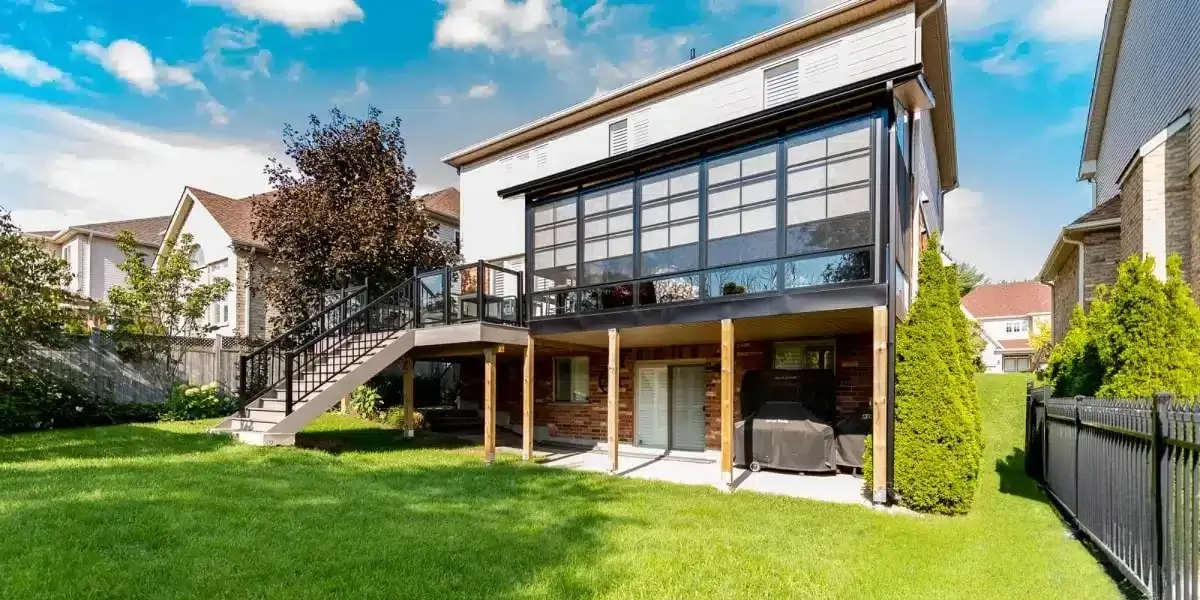 Sunspace WeatherMaster™ Model 200 enclosed sunroom with black aluminum framing, large vertical sliding windows, and an elevated deck with a staircase.