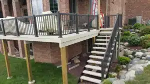 Elevated water-shedding deck with glass and metal railing, supported by wooden posts, creating a dry and stylish outdoor living space.