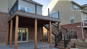 Elevated water-shedding deck with glass and metal railing, supported by wooden posts, creating a dry and stylish outdoor living space.