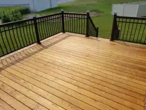 A beautiful Trex composite deck with a golden wood-look finish and black metal railing, overlooking a lush green lawn.