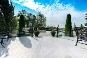 A stylish outdoor deck made with AlumaDeck decking, featuring a glass railing overlooking a luxurious backyard with a swimming pool, lush greenery, and a scenic landscape.