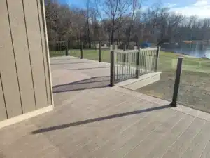 A spacious outdoor deck featuring a topless glass railing system with sturdy metal posts, overlooking a green lawn and a scenic river in the background.