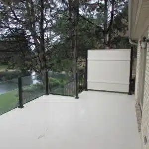 Modern topless glass railing system with black metal posts on an outdoor deck, offering a clear view of lush greenery and a serene waterfront