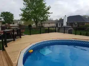 Spacious Trex Composite Decking in a natural wood finish surrounding an above ground pool, with black metal railing and a scenic backyard view.